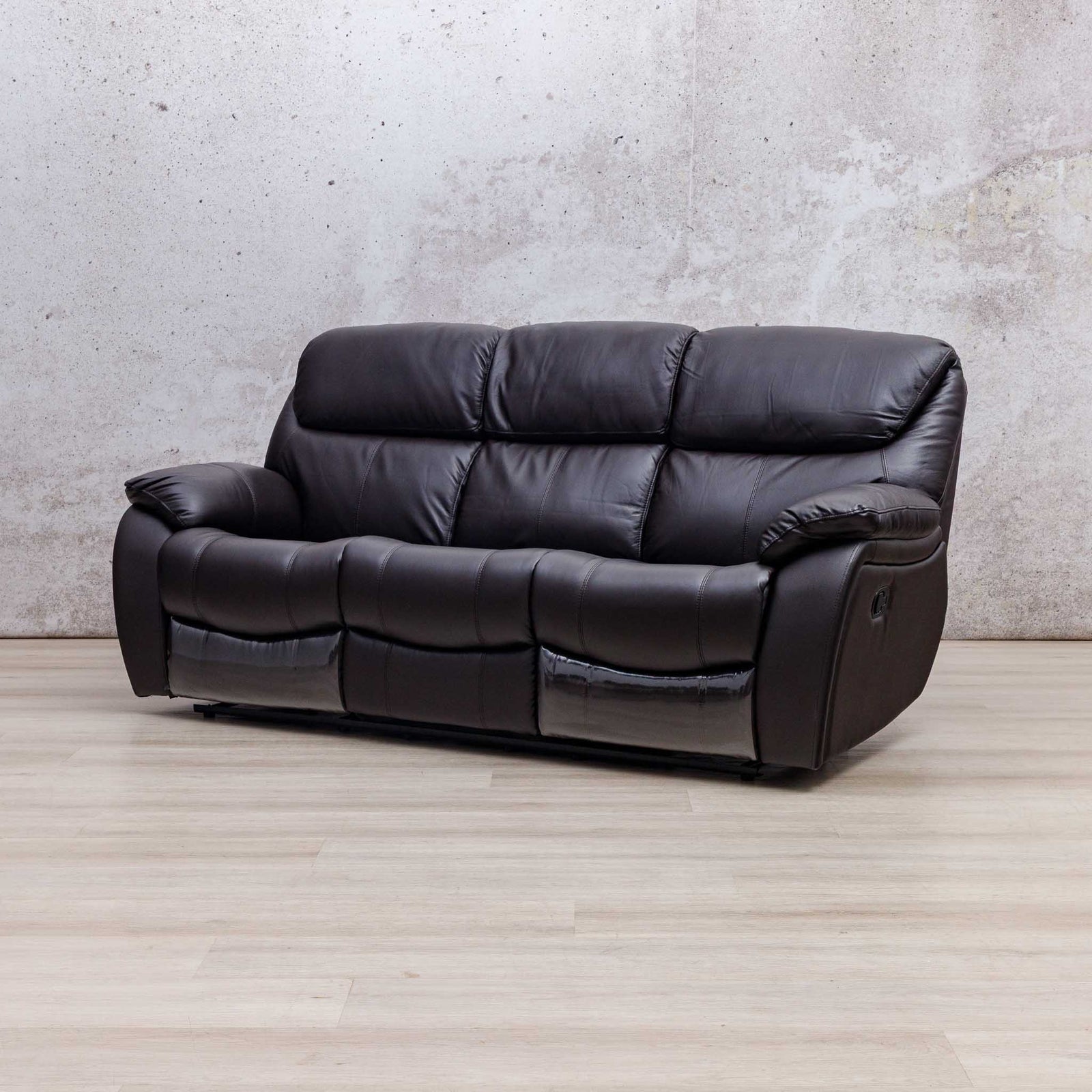 Leather Gallery Cairo 3 Seater Leather Recliner in Choc, shown in a modern room setting with a textured wall and light wood flooring.