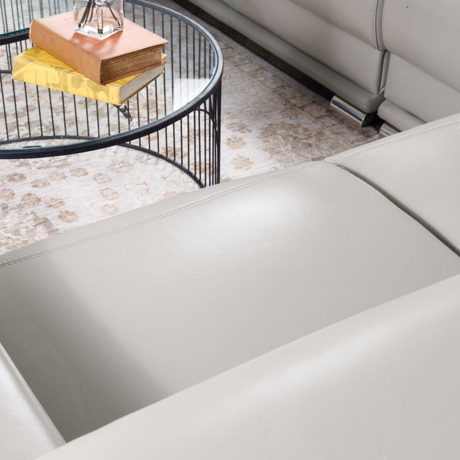 Close-up of the Leather Gallery Tobago 5 Seater Leather L Shape Couch in Grey, showing the leather armrest with a coffee table and patterned rug in the background.