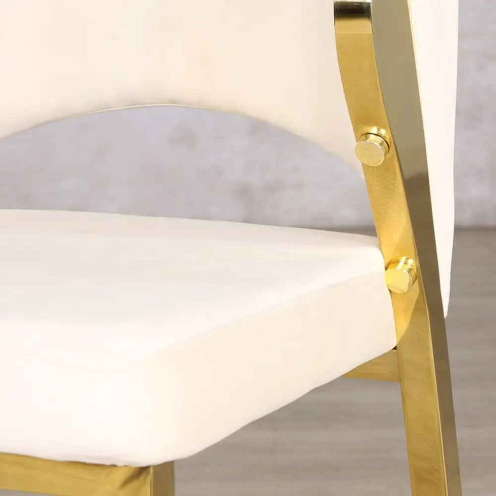 Close-up of the Cleopatra gold dining chair showcasing its sculptural gold stainless steel base and cream upholstered seat.