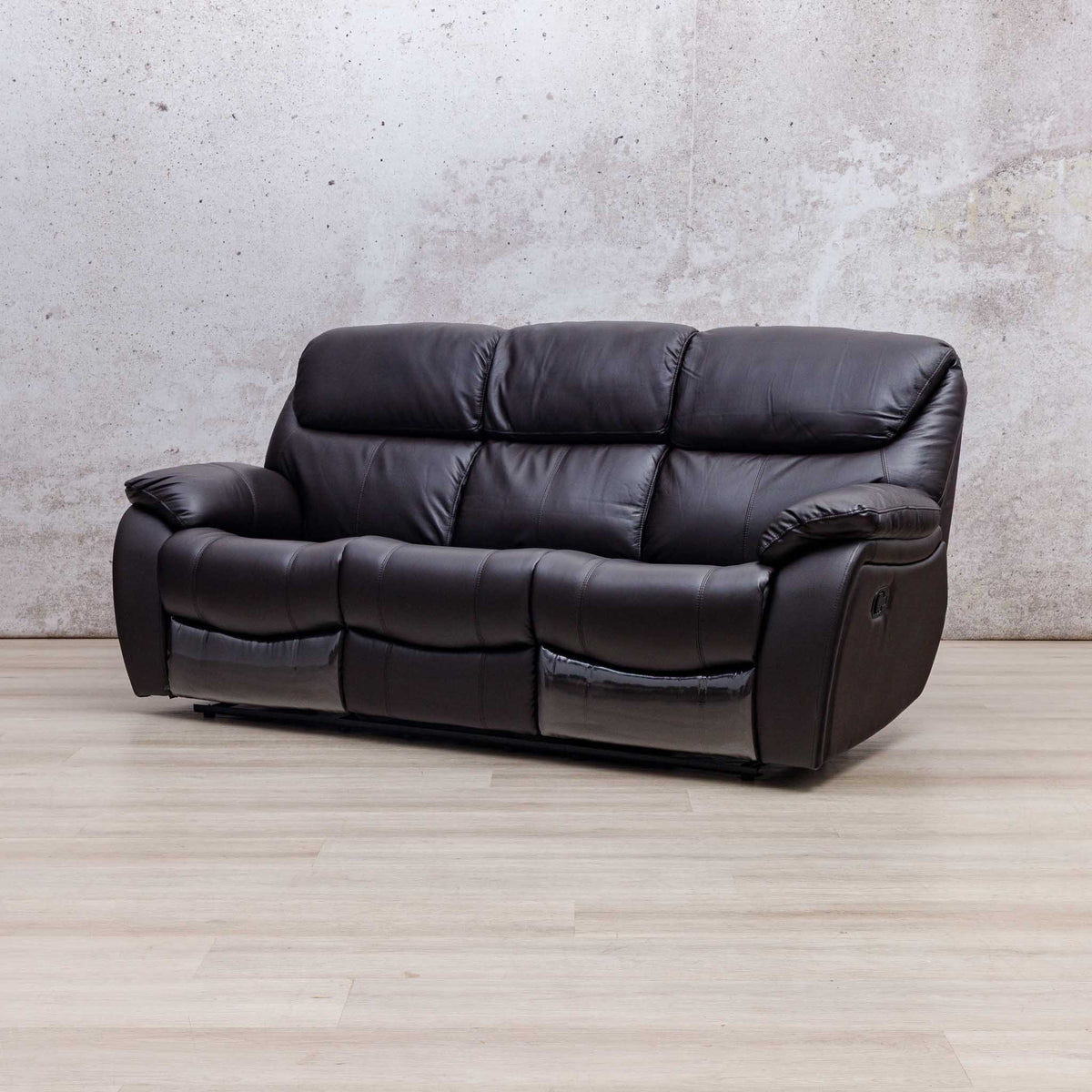 Leather Gallery Cairo 3 Seater Leather Recliner in Choc, shown in a modern room setting with a textured wall and light wood flooring.