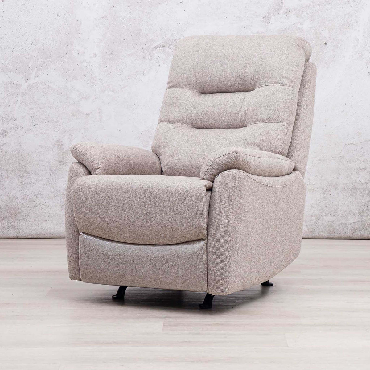 A modern upholstered recliner chair in a light beige textured fabric, shown in a relaxed reclined position on a light wood floor against a textured concrete wall.