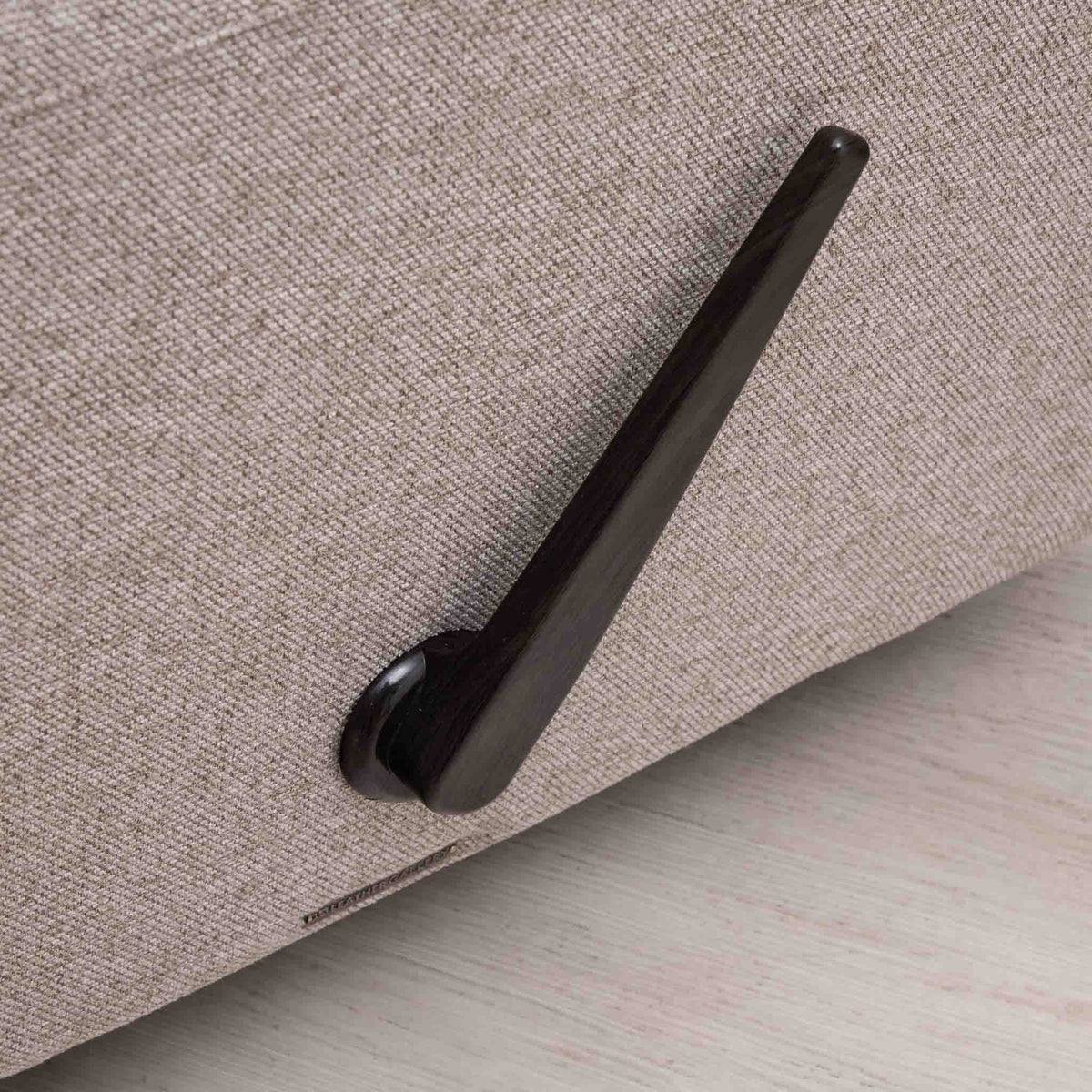 Close-up of the Leather Gallery Dallas Fabric Rocker Recliner Chair in Beige, showing the upholstered corner and curved dark metal recliner handle.