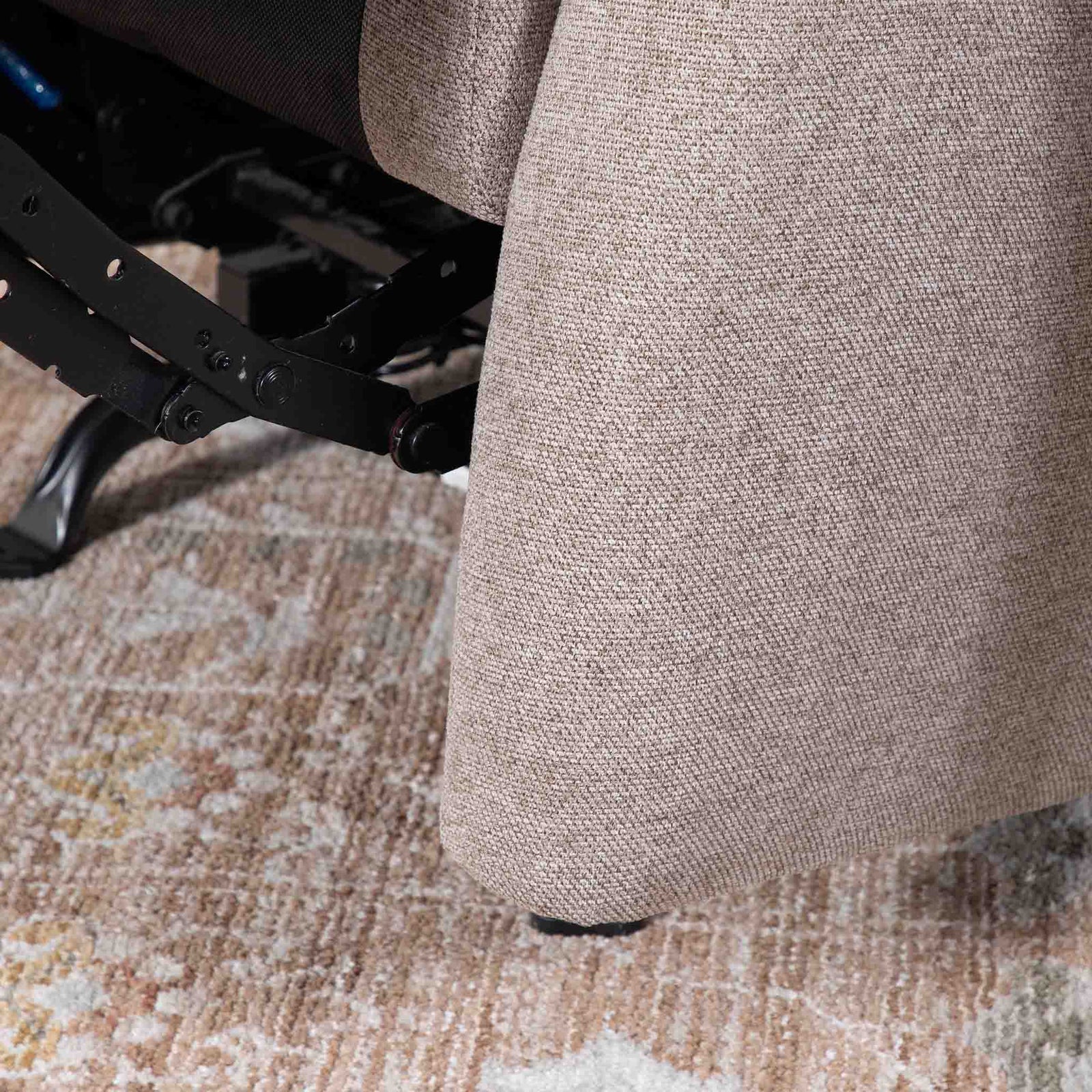 Close-up of the Leather Gallery Dallas Fabric Rocker Recliner Chair in Beige, showing the textured upholstery, armrest, and black metal support frame.