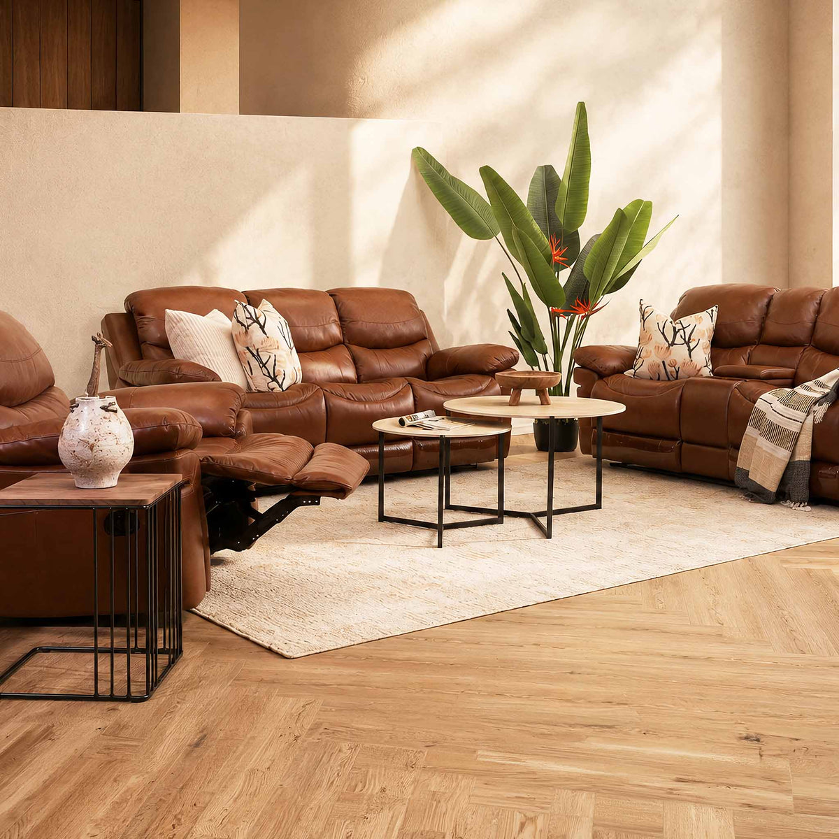 Brown leather sectional sofa with a matching recliner, neutral throw pillows, beige rug, round coffee tables, and a large potted plant.