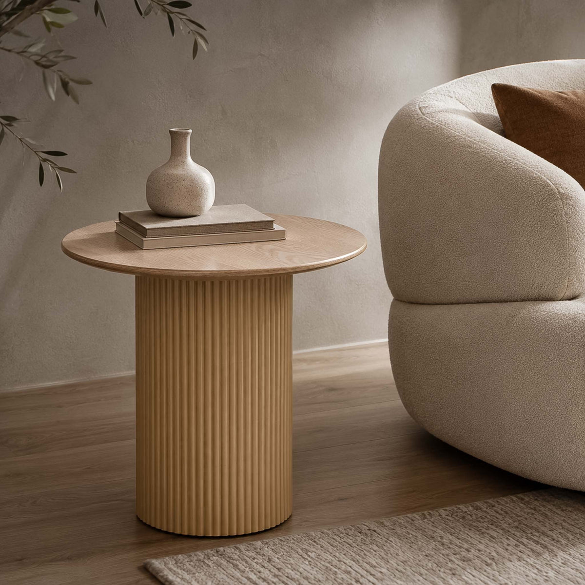 Gallery Everyday Sybil Side Table in Natural, featuring a round wooden top and fluted pedestal base styled beside a beige armchair.