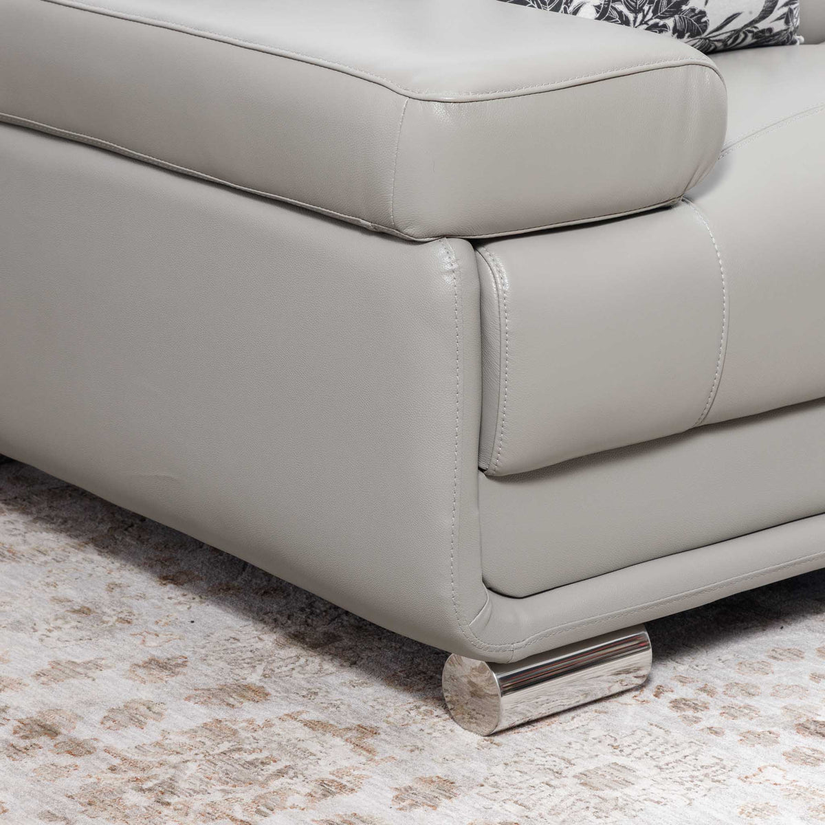 Close-up of the Leather Gallery Tobago 3 Seater Leather Couch in Grey, showing the leather corner, polished cylindrical metal foot, and patterned cushion.