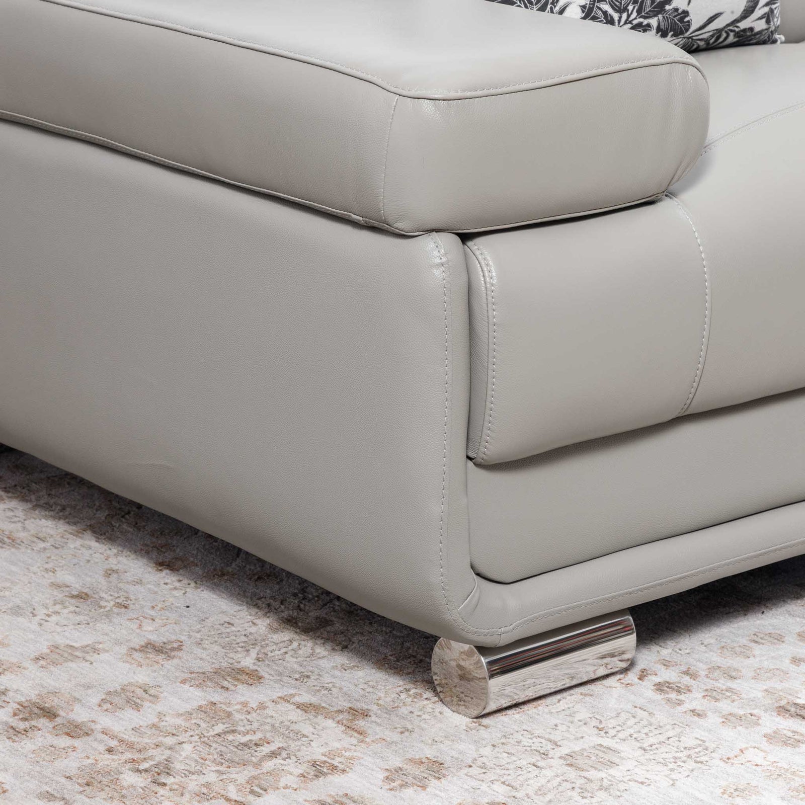 Close-up of the Leather Gallery Tobago 3 Seater Leather Couch in Grey, showing the leather corner, polished cylindrical metal foot, and patterned cushion.