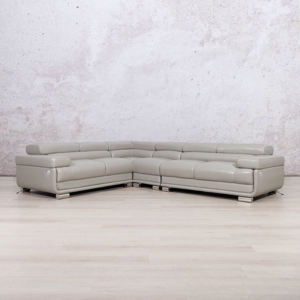 A light gray leather sectional sofa with a U-shape design, positioned on a light wood floor against a textured gray wall.