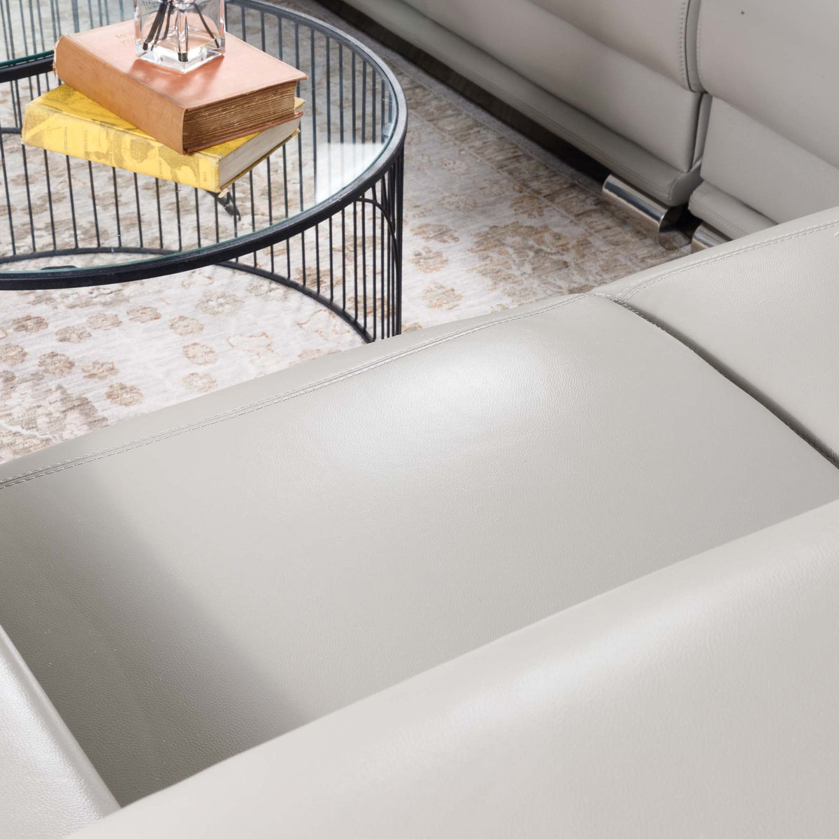Close-up of the Leather Gallery Tobago 5 Seater Leather L Shape Couch in Grey, showing the leather armrest with a coffee table and patterned rug in the background.