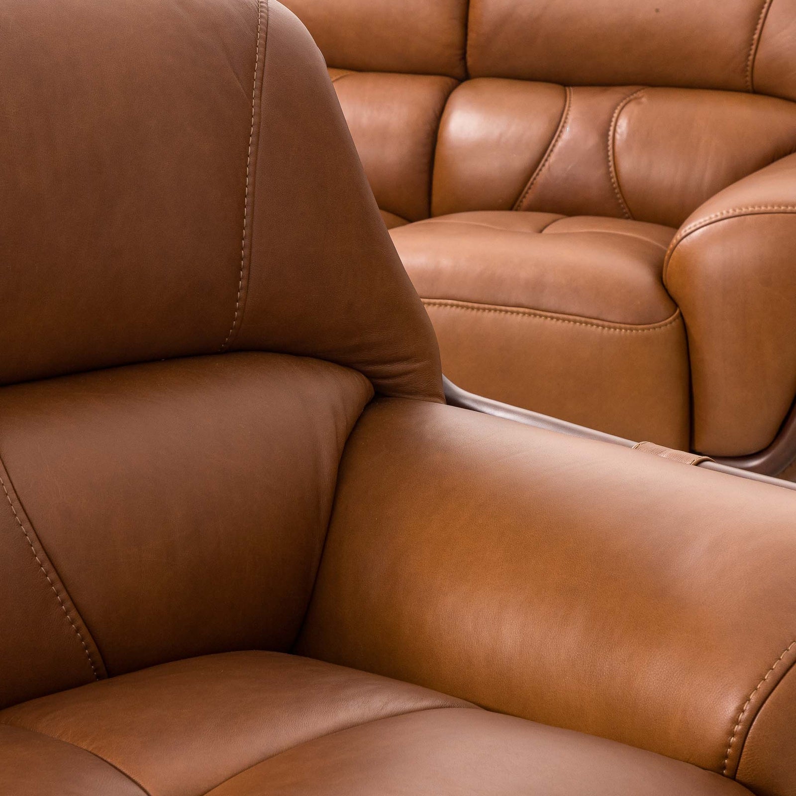 Close-up of the Leather Gallery Zuri 3+2+1 Leather Couch Suite in Czar Pecan, showing smooth leather texture, stitching, and a matching sofa in the background.