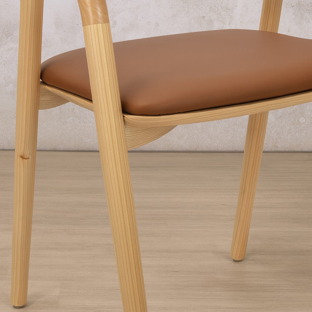 Close-up detail of the genuine leather upholstery on the seat of an Alaric wood dining chair, in a natural finish. 
