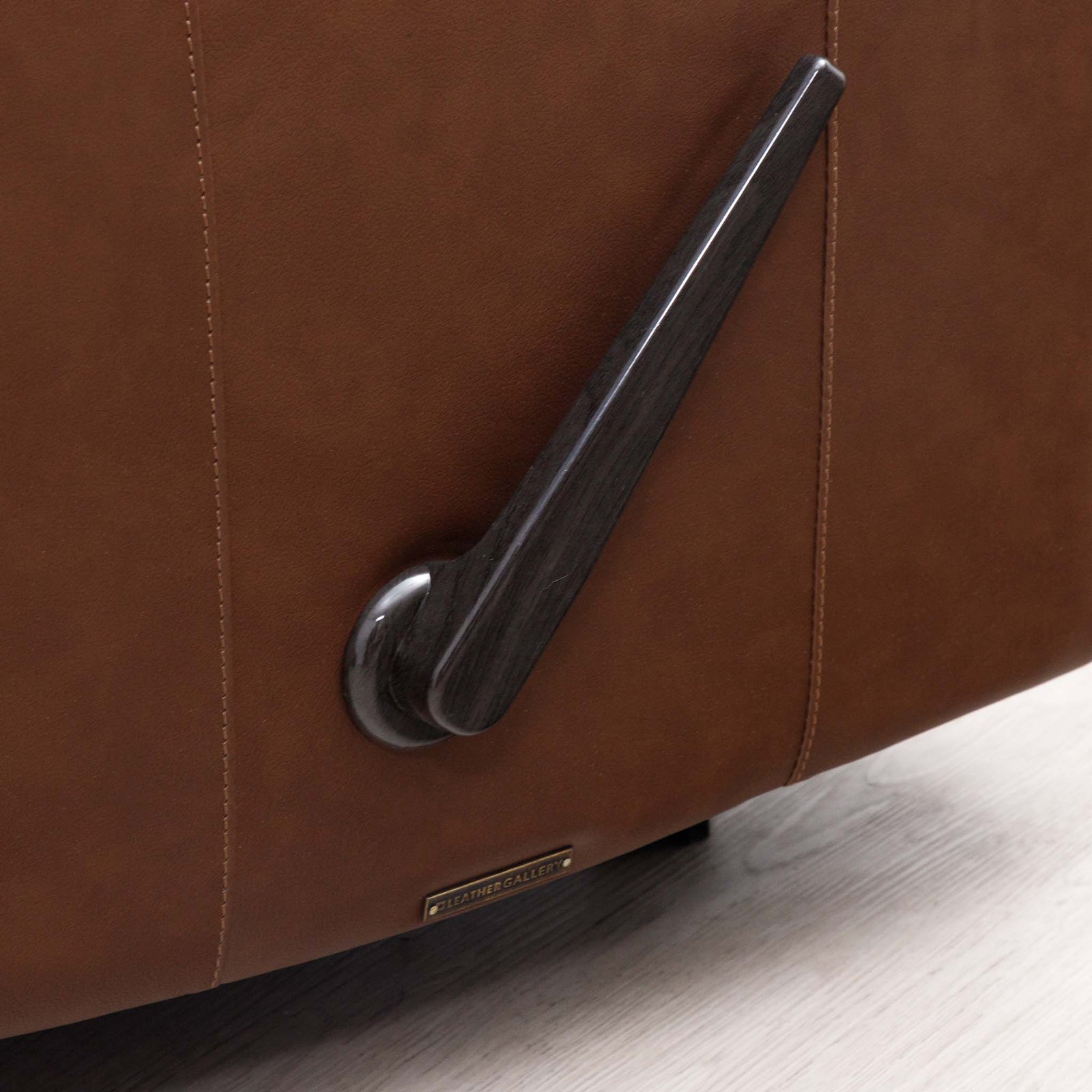 Close-up of the Leather Gallery Dallas Leather Rocker Recliner Chair in Saddle, showing the recline lever and gold-tone brand plaque.