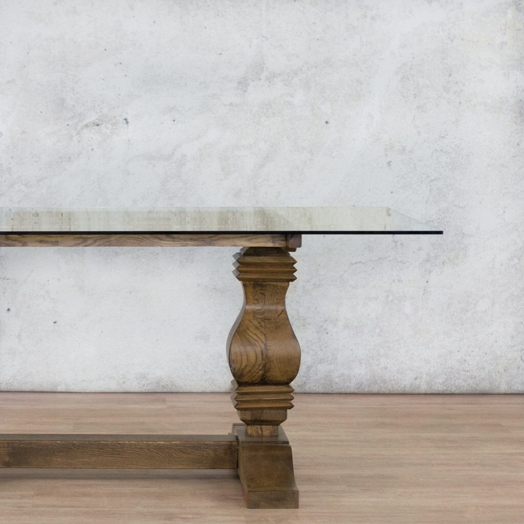 Close-up view of the Belmont Glass Top Dining Table – 2.4m / 8-10 Seater in Antique Dark Oak, showcasing the fine detailing of the wooden base and clear glass top. Leather Gallery--antique-dark-oak
