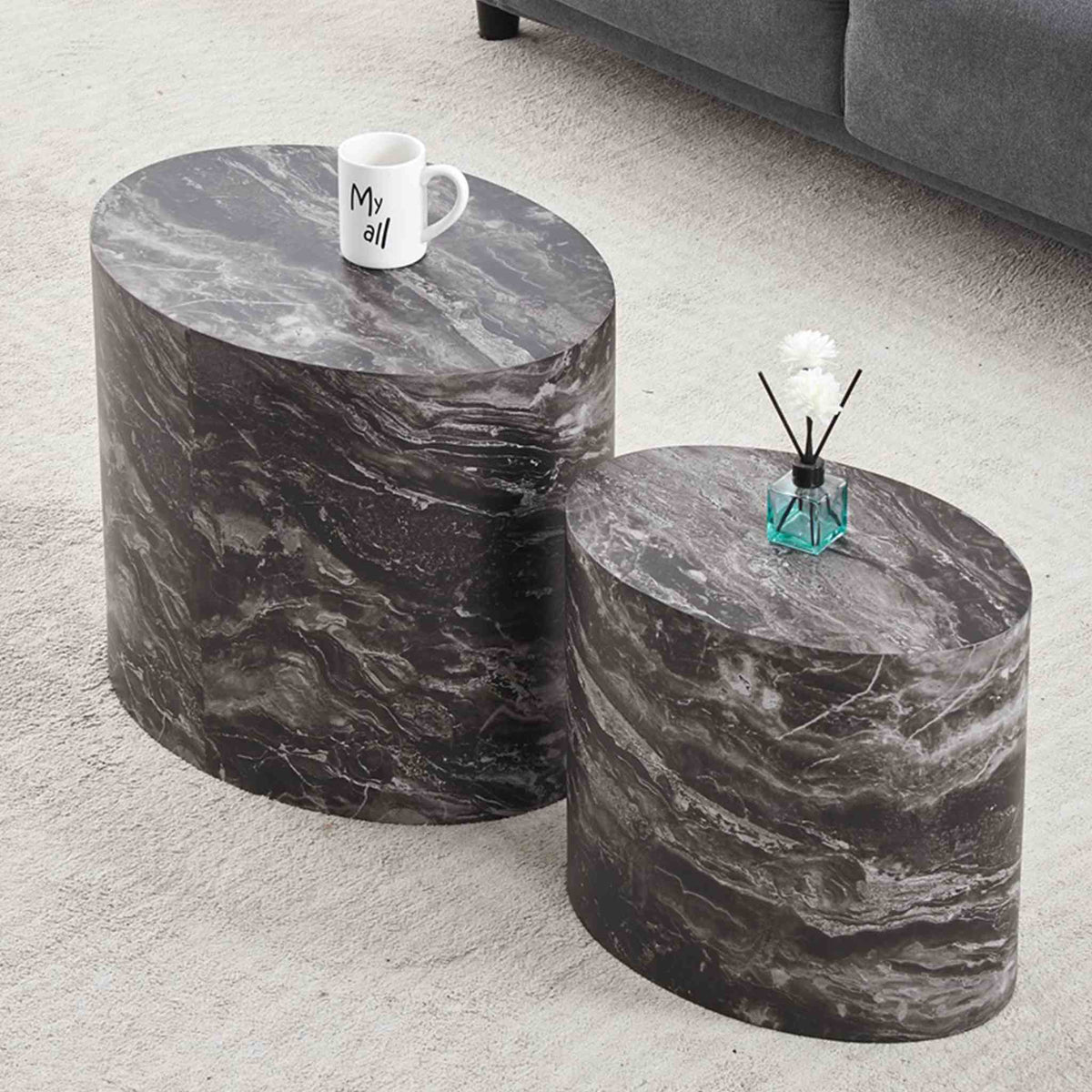 Gallery Everyday Callaway Coffee Table Set of 2, featuring cylindrical marble-look tables styled with a mug and small plant on a light grey carpet.