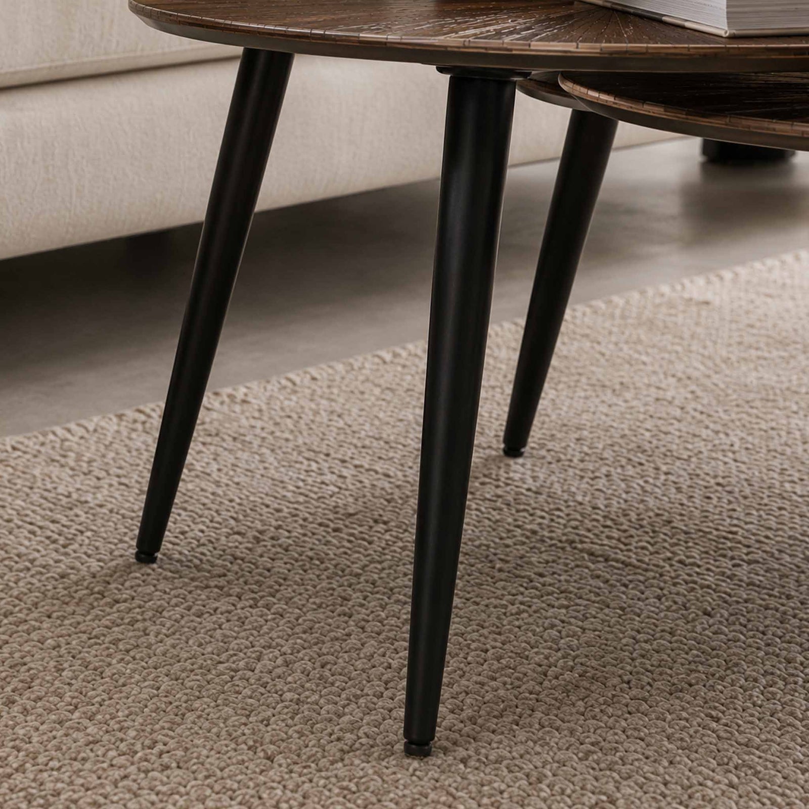 Close-up of the Gallery Everyday Eden Nesting Coffee Tables Set of 2, showing a round wooden top and tapered black metal legs.
