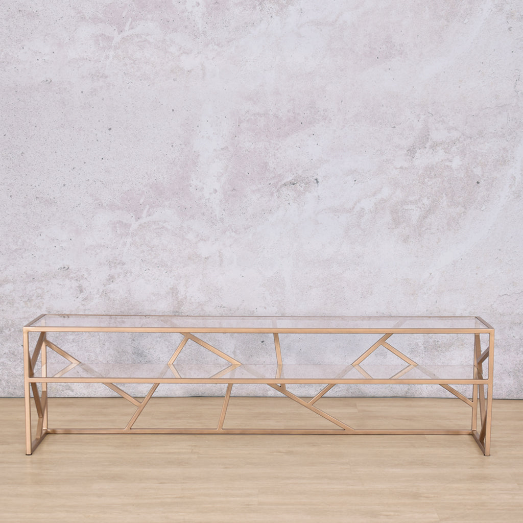 Front-facing view of the Legacy TV Unit, highlighting the geometric gold steel base and sleek glass shelf for storage