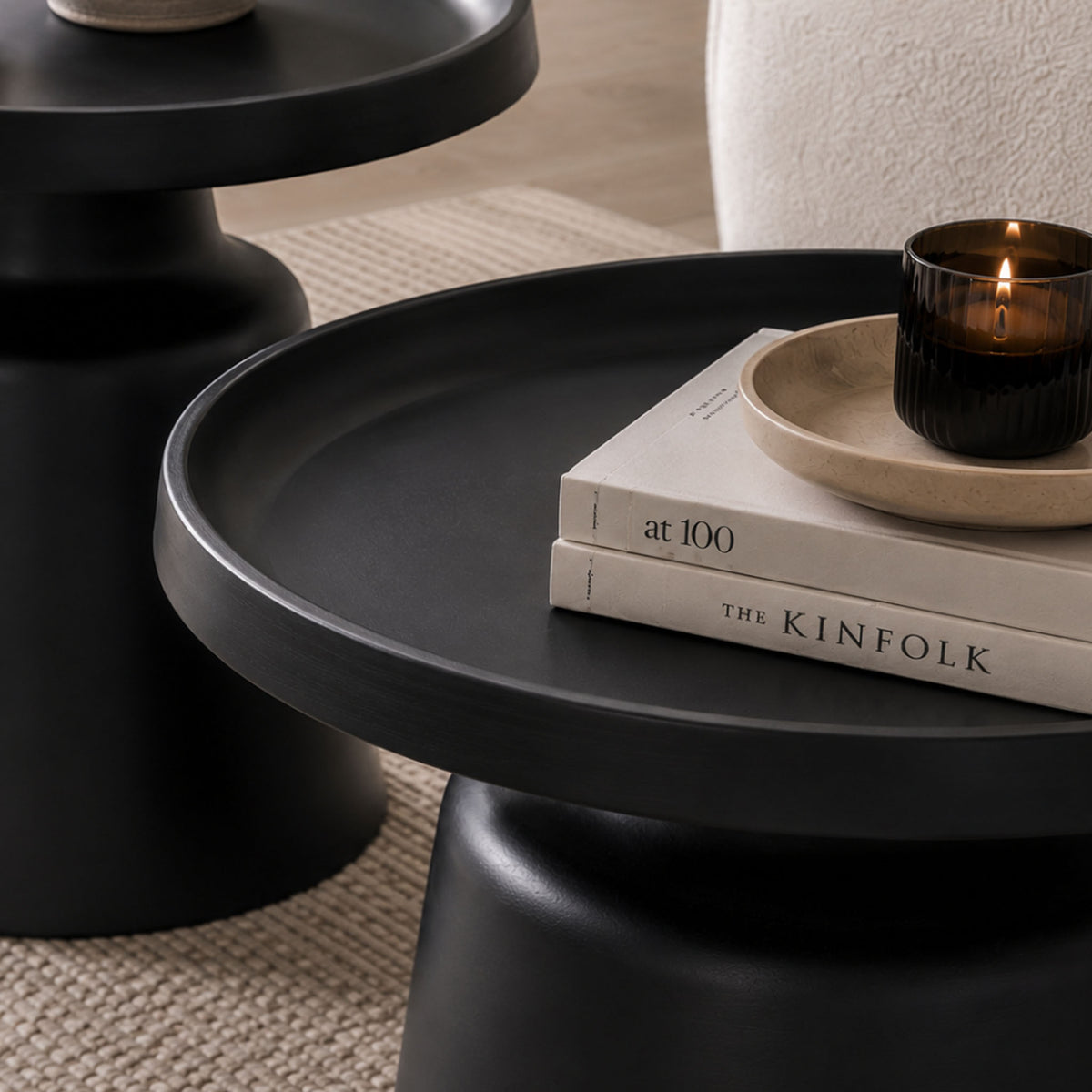 Close-up of the Gallery Everyday Minerva Coffee Table - Black Set of 2, showing a matte black pedestal table styled with books, a candle, and matching table in the background.