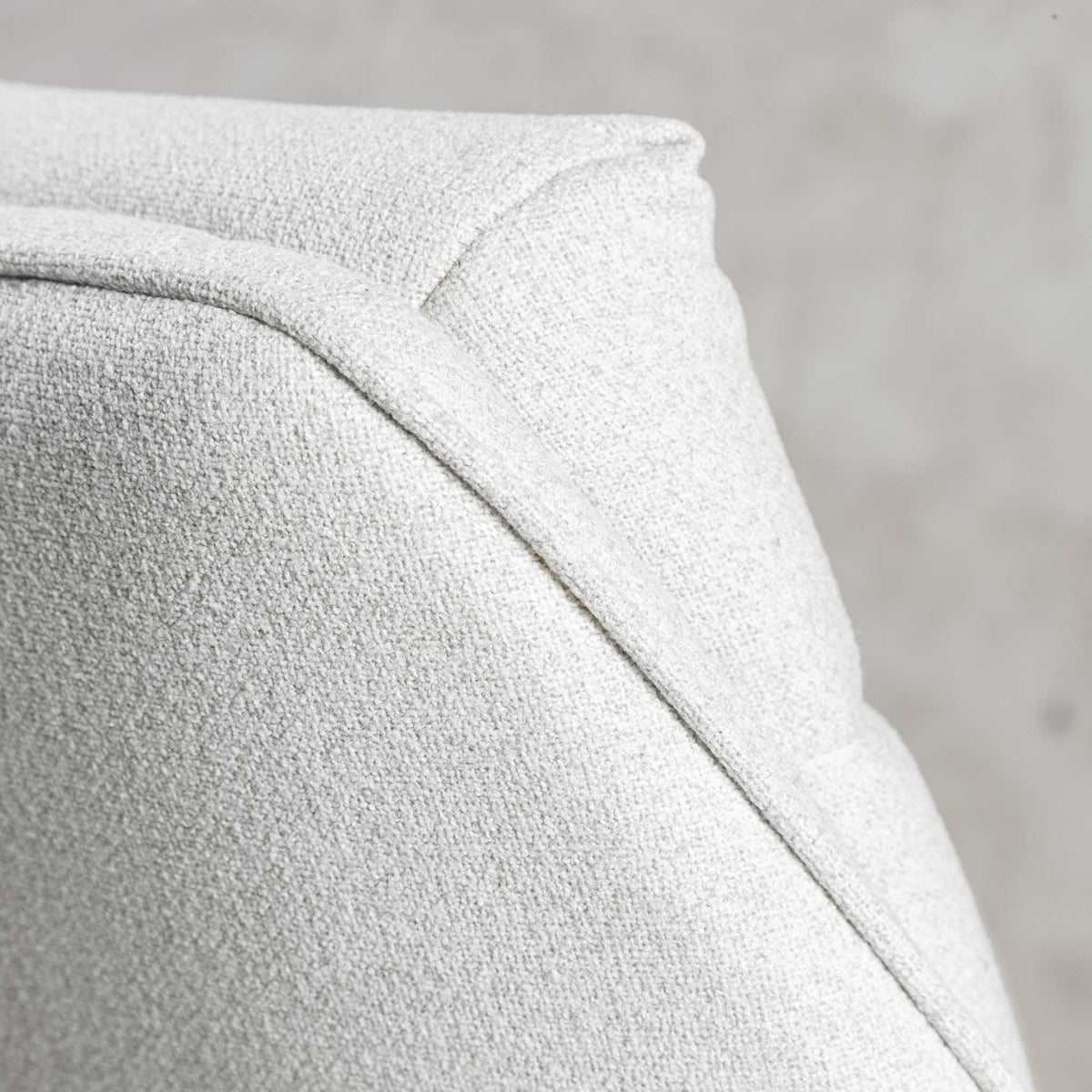Close-up of curved armrest on Octavia light grey fabric dining chair, showing piping detail. 